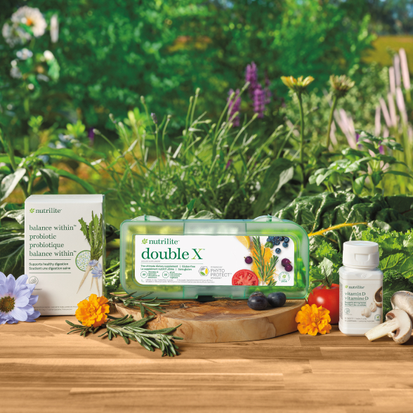 Nutrilite Balance Within Probiotic, Nutrilite Double X Multivitamin, and Nutrilite Vitamin D products on a wooden board, surrounded by florals and vegetables.