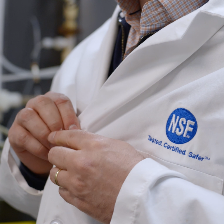 A scientist’s hands buttoning up a lab coat with a blue NSF logo on it.
